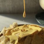 Cheesy Queso is drizzled over a pile of chips