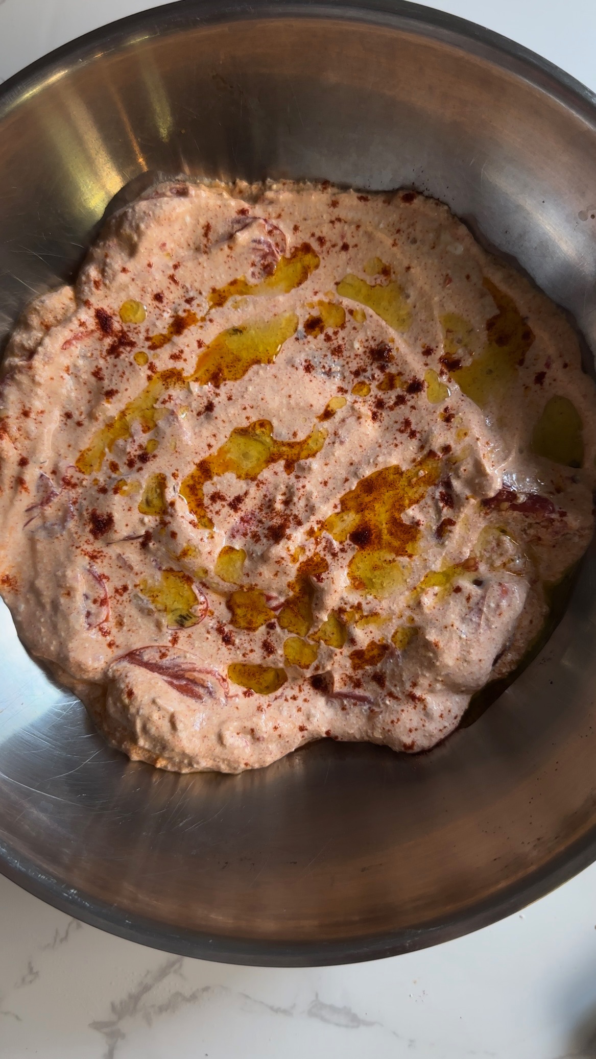 Cheesy dip with olive oil and paprika in a stainless steel bowl