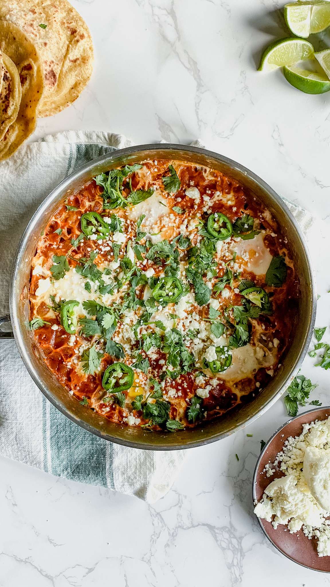 A pan of delicious eggs cooked in a tomato and enchilada sauce garnished with cilantro, jalepenos, and fresh corn tortillas.