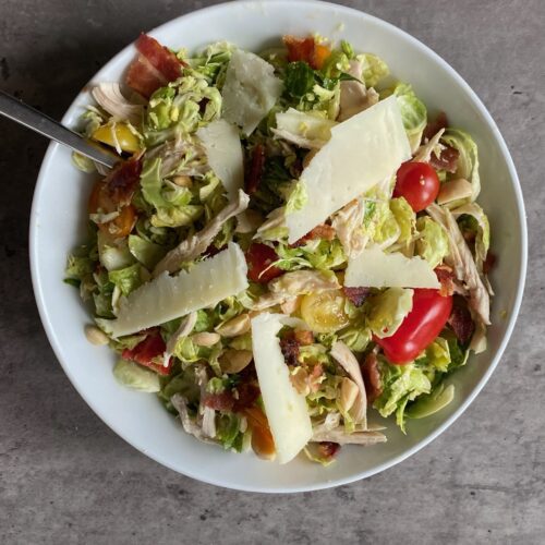 Brussels sprout salad with tomatoes, chicken and cheese slices served in a large bowl