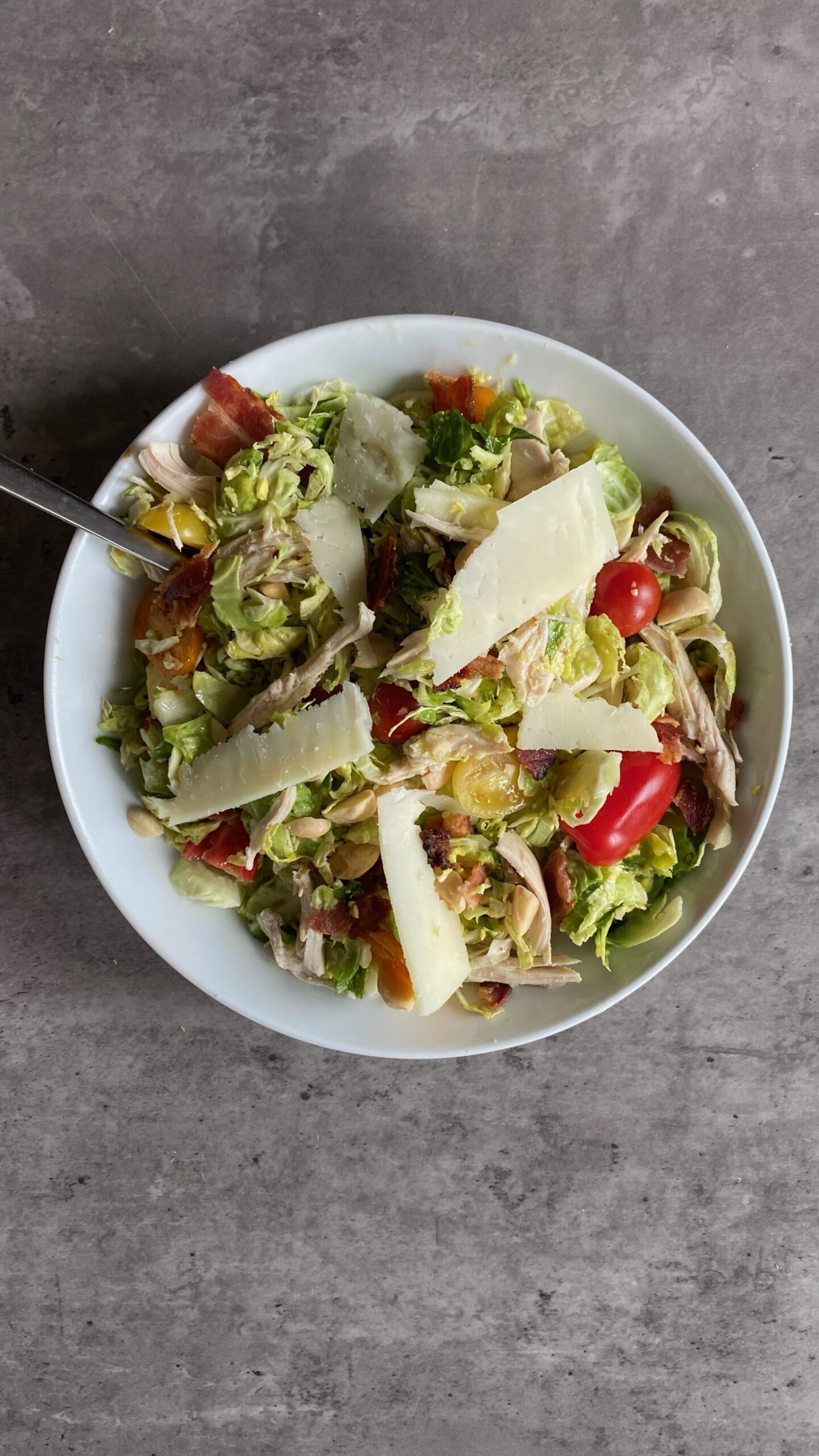 Brussels sprout salad with tomatoes, chicken and cheese slices served in a large bowl