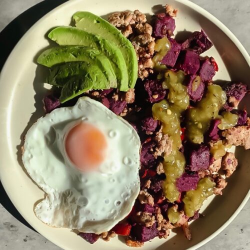 Breakfast hash with fried egg and avocado on plate with salt and pepper