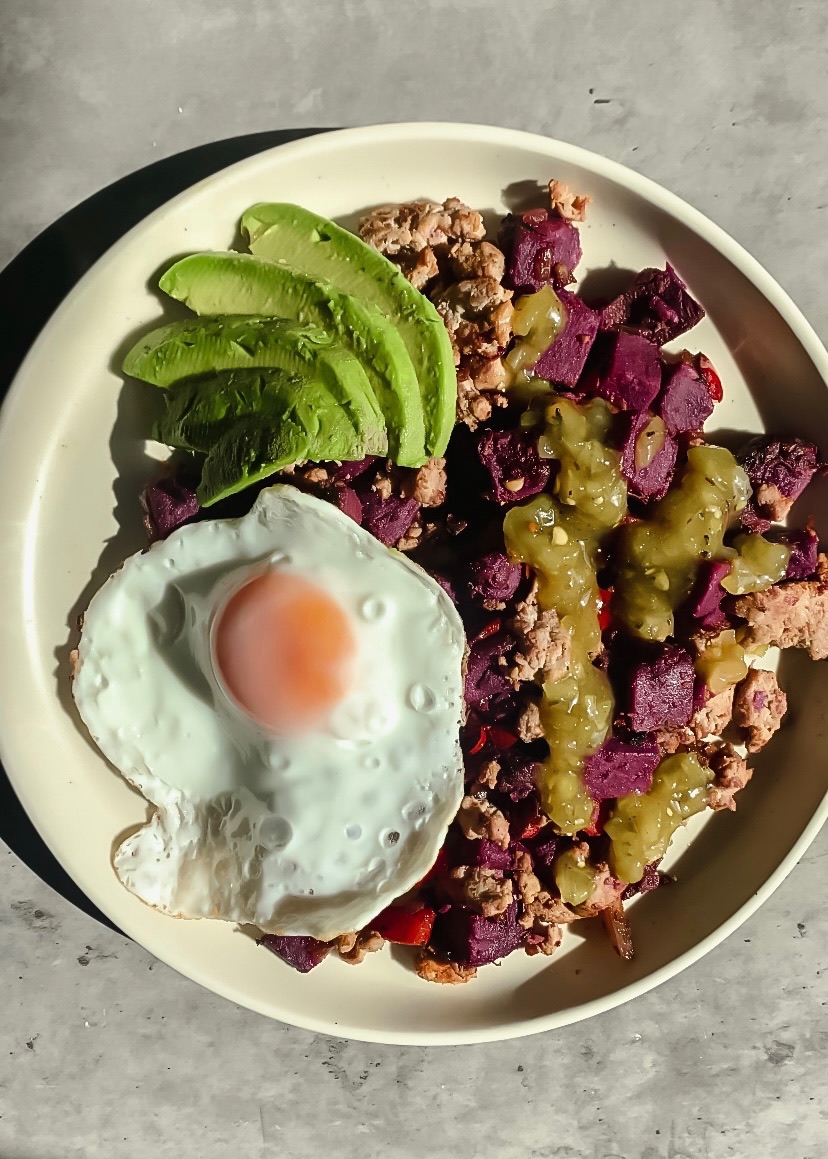 Breakfast hash with fried egg and avocado on plate with salt and pepper