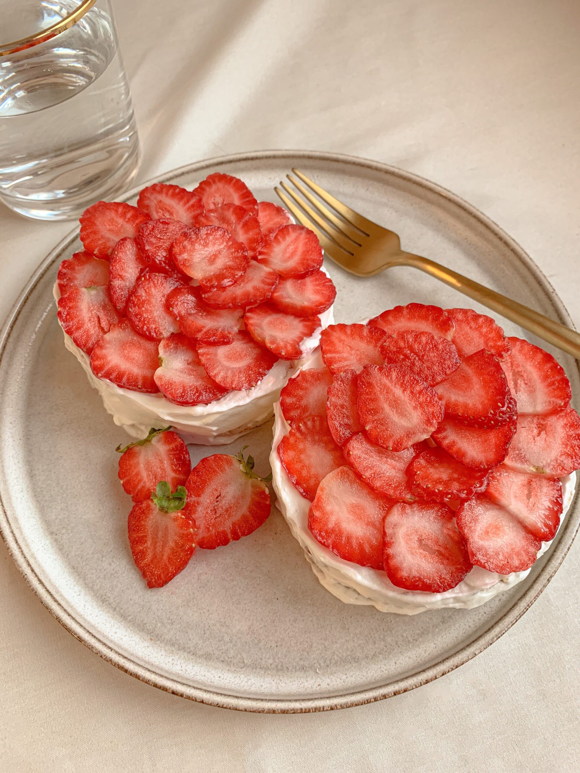 Two small white cakes are arranged on a plate and topped with vibrant red strawberry slices