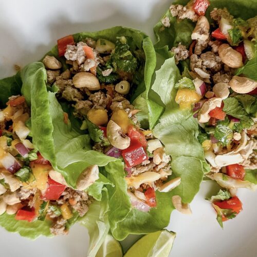 Three lettuce cups filled with a ground turkey and a colorful mango, bell pepper pico garnished with two lime wedges on the side