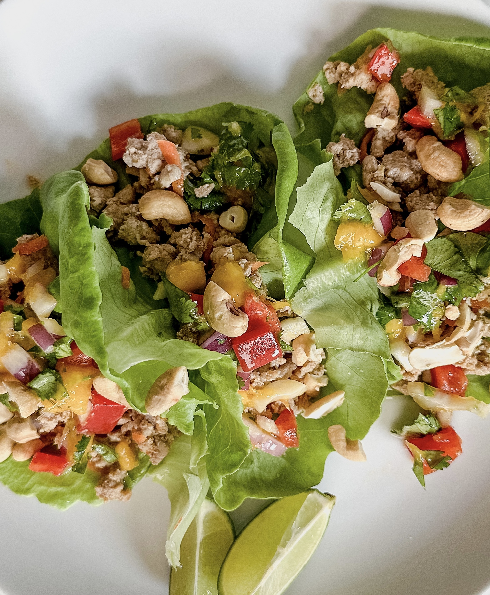 Three lettuce cups filled with a ground turkey and a colorful mango, bell pepper pico garnished with two lime wedges on the side